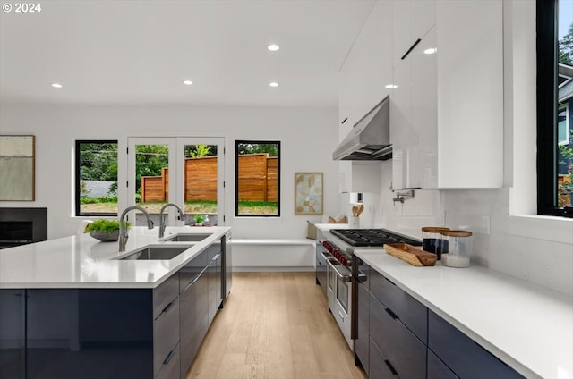 kitchen with white cabinetry, exhaust hood, light wood-type flooring, double oven range, and a kitchen island with sink