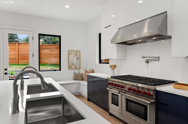 kitchen with white cabinetry, wall chimney exhaust hood, light hardwood / wood-style flooring, double oven range, and sink