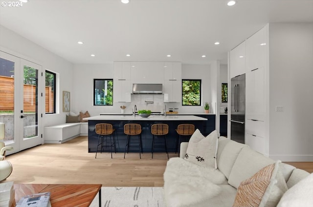 kitchen featuring exhaust hood, a center island with sink, and white cabinetry