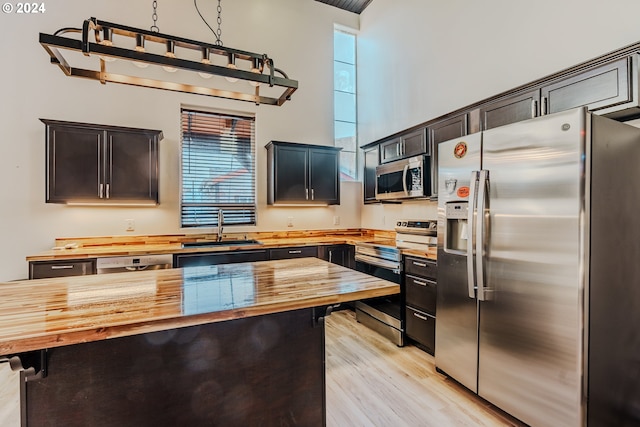 kitchen featuring sink, light hardwood / wood-style flooring, appliances with stainless steel finishes, a kitchen island, and butcher block counters