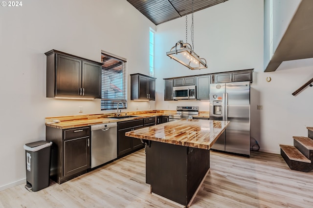 kitchen featuring a center island, hanging light fixtures, stainless steel appliances, a high ceiling, and wood counters