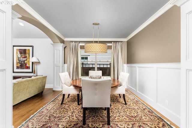 dining room featuring arched walkways, wood finished floors, crown molding, and decorative columns