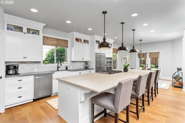 kitchen with a sink, a center island, appliances with stainless steel finishes, light wood finished floors, and decorative backsplash