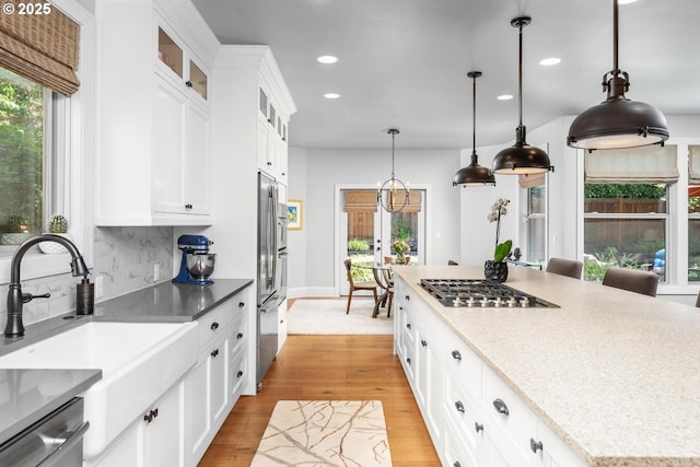 kitchen with light wood-type flooring, decorative backsplash, appliances with stainless steel finishes, hanging light fixtures, and a sink