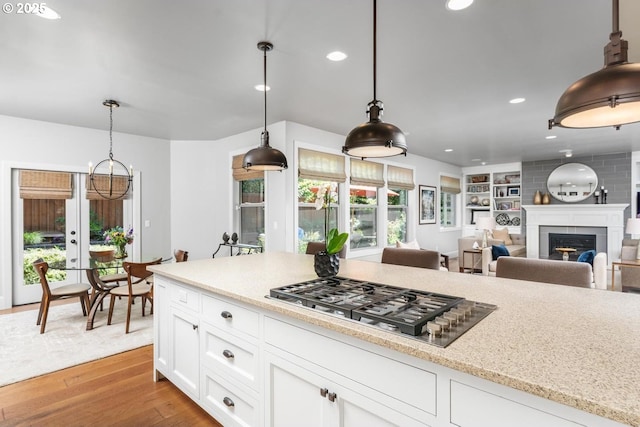 kitchen with stainless steel gas stovetop, pendant lighting, a fireplace, wood finished floors, and white cabinetry