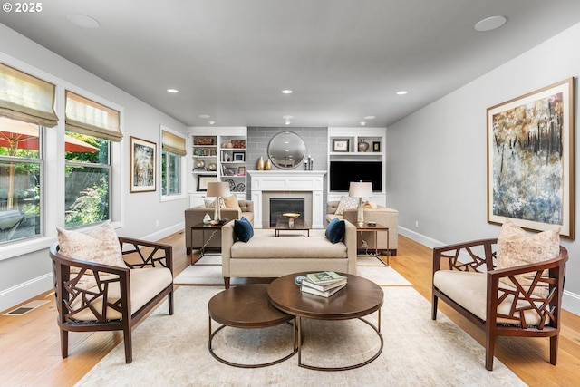 living area featuring visible vents, built in features, recessed lighting, light wood-style flooring, and a fireplace