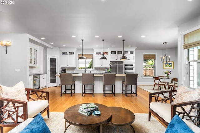 living room featuring beverage cooler, recessed lighting, light wood-style flooring, and an inviting chandelier