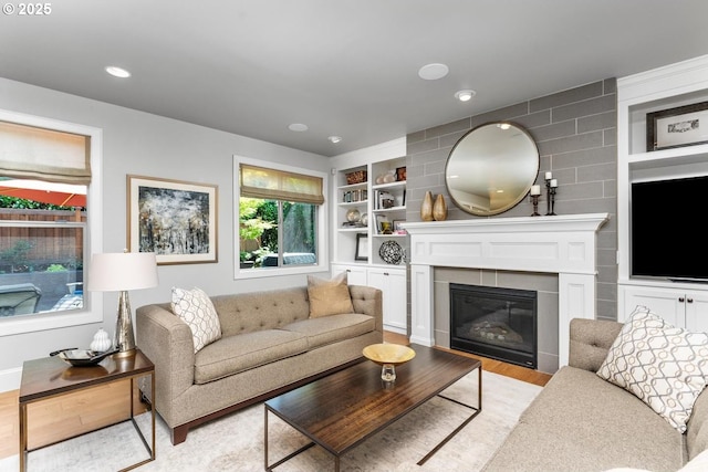 living area with recessed lighting, built in shelves, a glass covered fireplace, and light wood finished floors