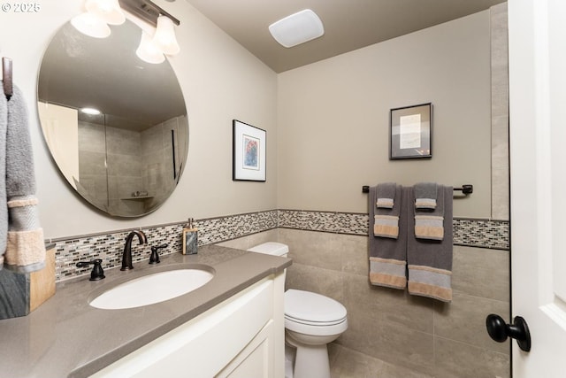 full bath with tile patterned flooring, a wainscoted wall, toilet, vanity, and tile walls