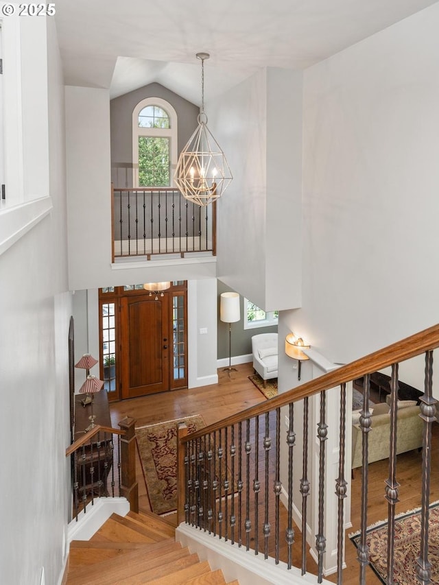 staircase with baseboards, a notable chandelier, wood finished floors, and high vaulted ceiling