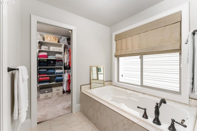 full bathroom featuring a walk in closet, a garden tub, and marble finish floor