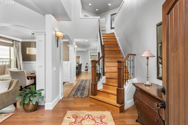 foyer entrance with a wainscoted wall, light wood-style flooring, stairway, arched walkways, and decorative columns