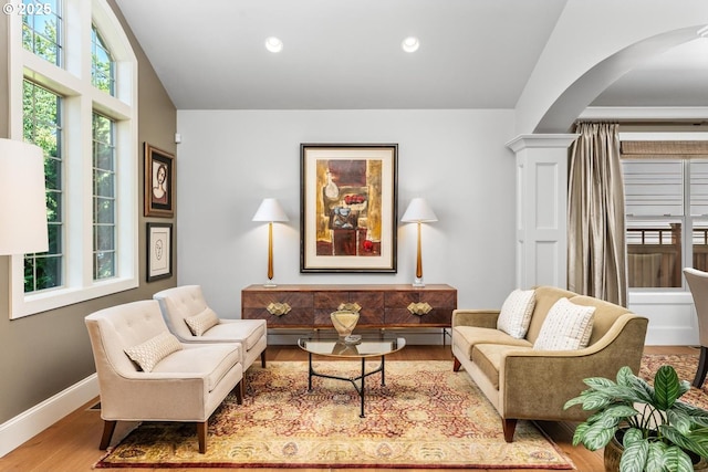 living area featuring wood finished floors, recessed lighting, arched walkways, decorative columns, and baseboards