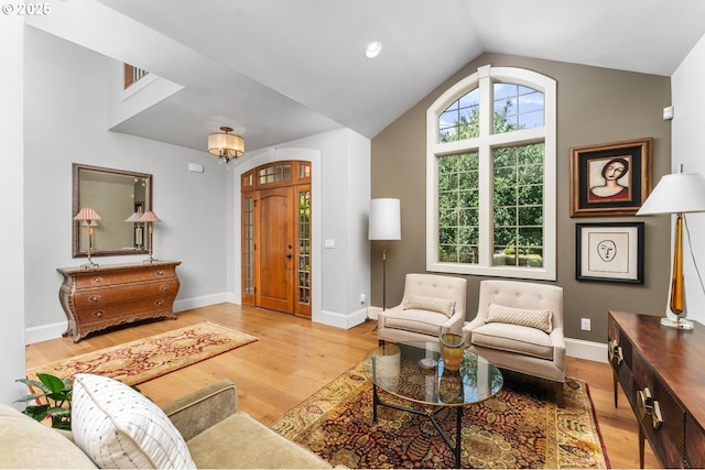 living area with baseboards, light wood-type flooring, and lofted ceiling