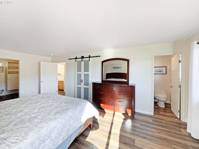 bedroom with a barn door, ensuite bath, and dark hardwood / wood-style floors