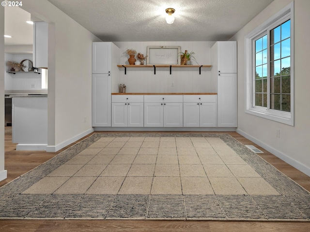 interior space featuring white cabinets, light hardwood / wood-style floors, and a textured ceiling