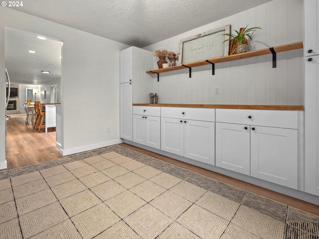 interior space featuring a textured ceiling, wooden walls, light hardwood / wood-style floors, and white cabinetry