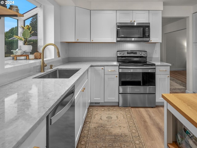 kitchen featuring white cabinets, sink, stainless steel appliances, light stone countertops, and light hardwood / wood-style floors