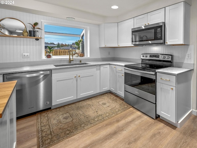 kitchen with white cabinets, butcher block countertops, stainless steel appliances, light wood-type flooring, and sink