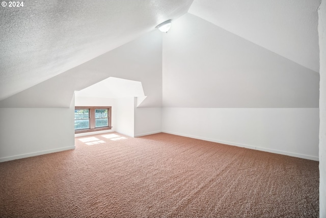 additional living space featuring carpet flooring, vaulted ceiling, and a textured ceiling