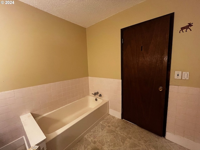 bathroom featuring a washtub, a textured ceiling, tile patterned floors, and tile walls