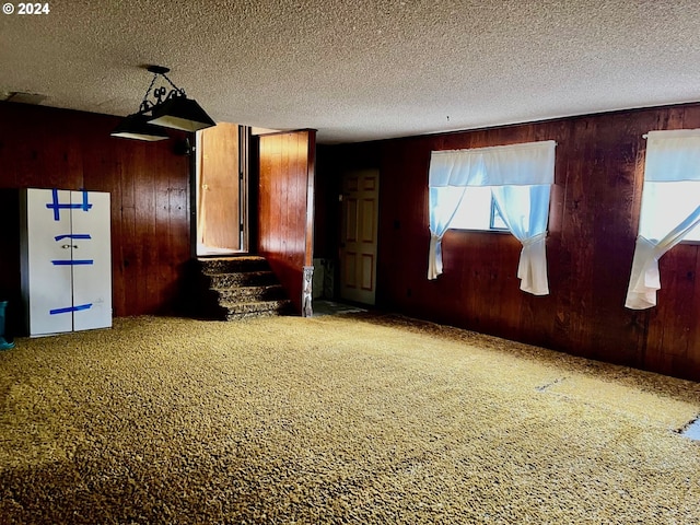 carpeted empty room with wooden walls and a textured ceiling