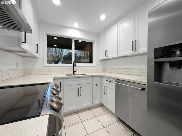 kitchen with sink, wall chimney exhaust hood, light tile patterned floors, white cabinetry, and stainless steel appliances