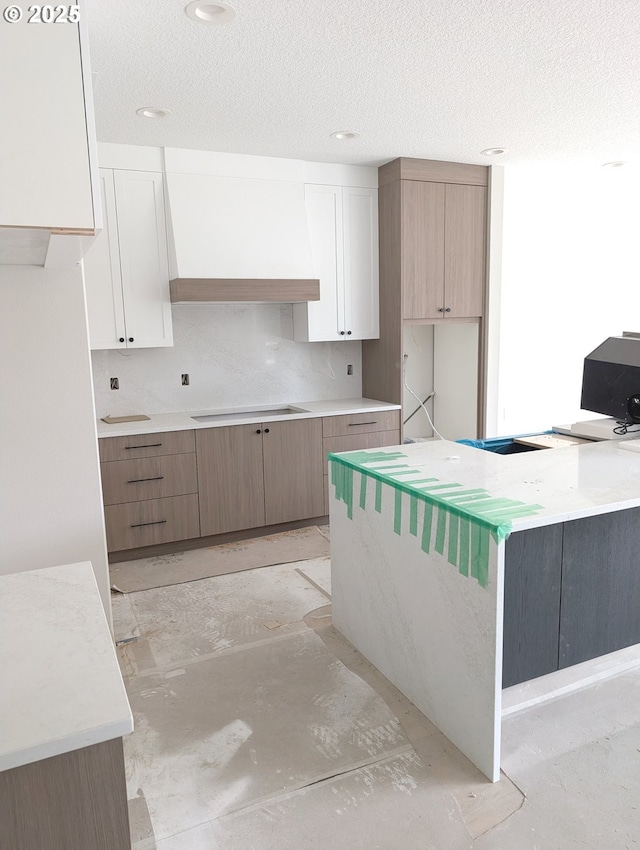 kitchen featuring unfinished concrete floors, cooktop, custom range hood, and a textured ceiling