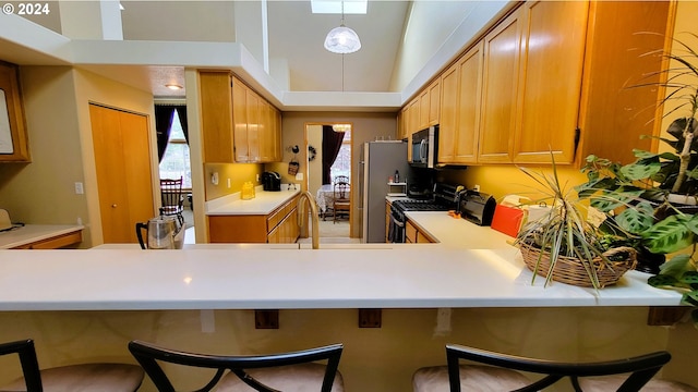 kitchen with hanging light fixtures, kitchen peninsula, a towering ceiling, a breakfast bar, and appliances with stainless steel finishes