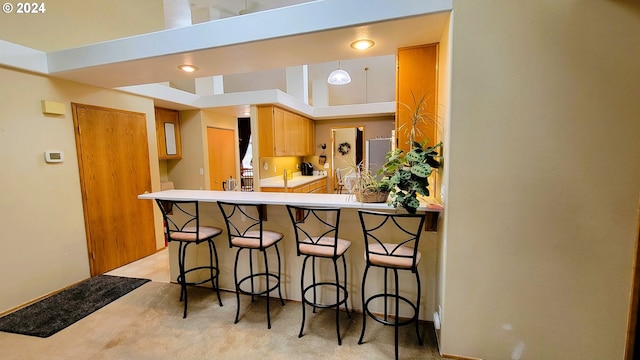 kitchen featuring kitchen peninsula, light carpet, a breakfast bar, and a towering ceiling