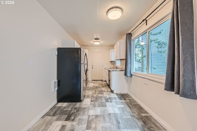 kitchen featuring light hardwood / wood-style floors, stainless steel refrigerator, sink, light stone countertops, and white cabinets