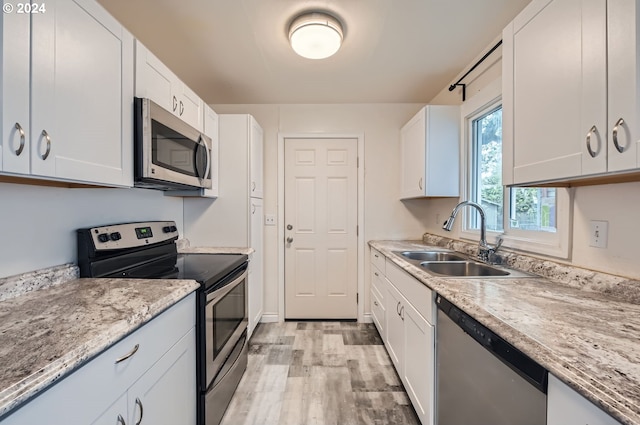 kitchen with light hardwood / wood-style floors, sink, light stone counters, white cabinets, and appliances with stainless steel finishes