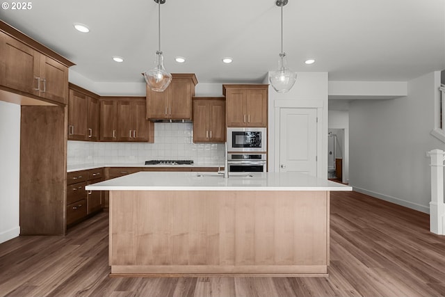 kitchen with dark hardwood / wood-style floors, stainless steel appliances, decorative light fixtures, and an island with sink