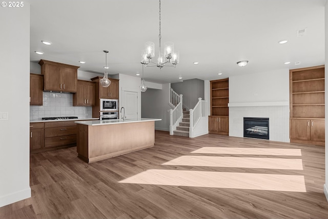 kitchen with sink, hanging light fixtures, stainless steel appliances, a center island with sink, and light wood-type flooring