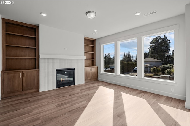 unfurnished living room featuring a tile fireplace, built in features, and light wood-type flooring