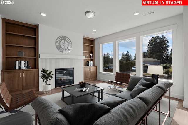 living room featuring built in shelves, a fireplace, light hardwood / wood-style flooring, and a wealth of natural light