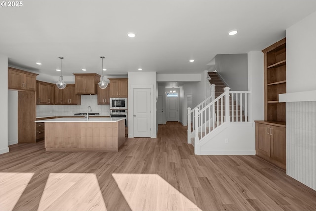 kitchen featuring pendant lighting, black microwave, light hardwood / wood-style floors, an island with sink, and stainless steel oven