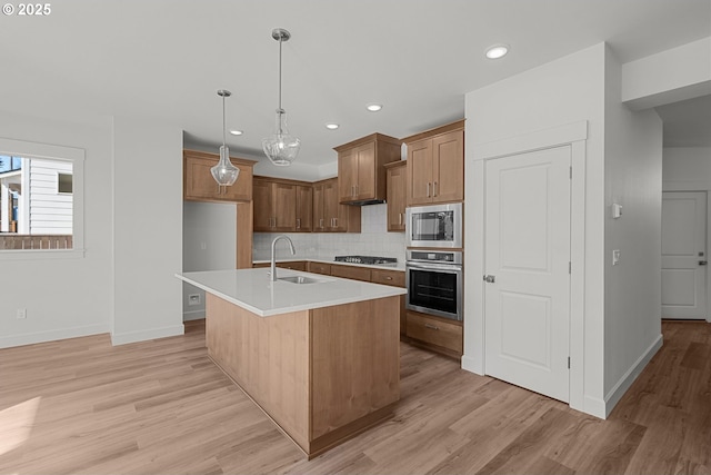 kitchen with sink, appliances with stainless steel finishes, backsplash, hanging light fixtures, and a center island with sink