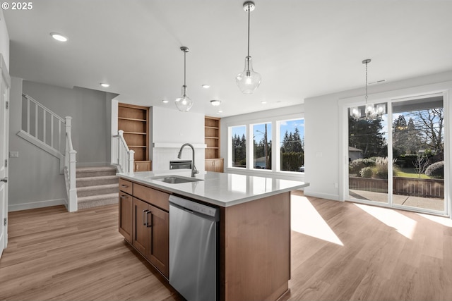 kitchen featuring pendant lighting, sink, light hardwood / wood-style flooring, a center island with sink, and stainless steel dishwasher