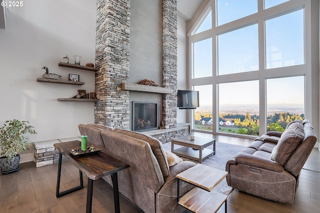 living room with a stone fireplace, a towering ceiling, and wood-type flooring