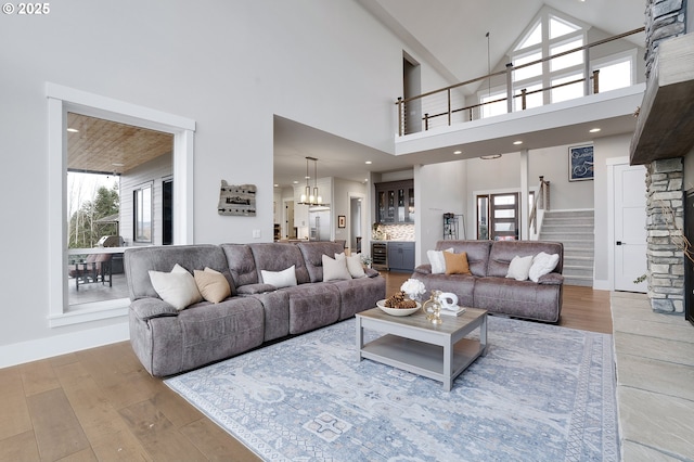 living area with a chandelier, high vaulted ceiling, wood finished floors, and stairs