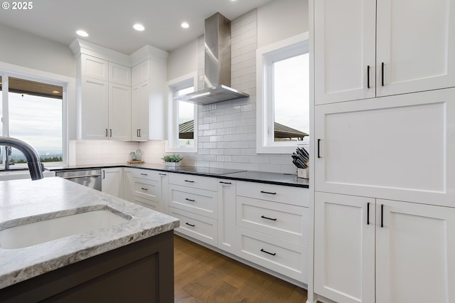 kitchen with white cabinets, dark stone counters, wall chimney exhaust hood, and sink