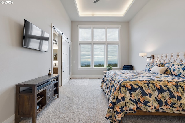 bedroom with a barn door, light carpet, and a tray ceiling