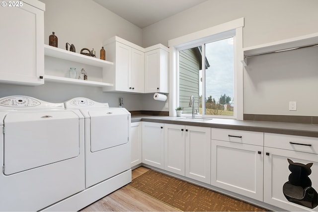 laundry room featuring washing machine and dryer, sink, cabinets, and light hardwood / wood-style floors