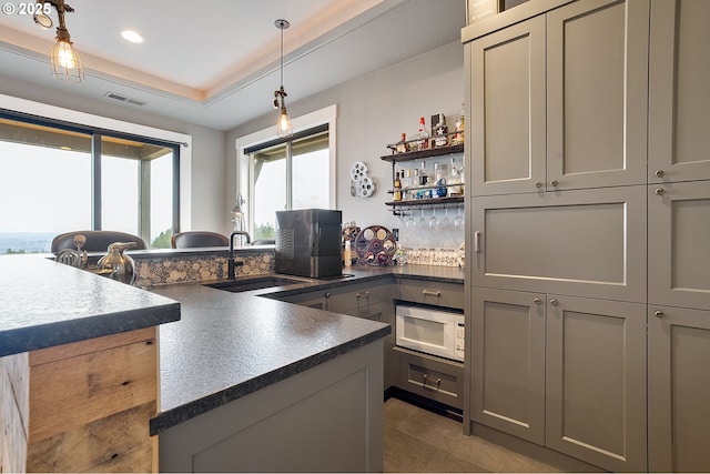 kitchen with sink, hanging light fixtures, an island with sink, gray cabinets, and white microwave