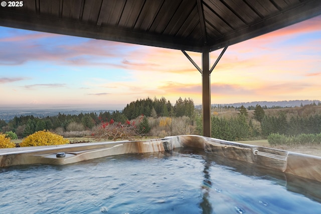 pool at dusk featuring a hot tub