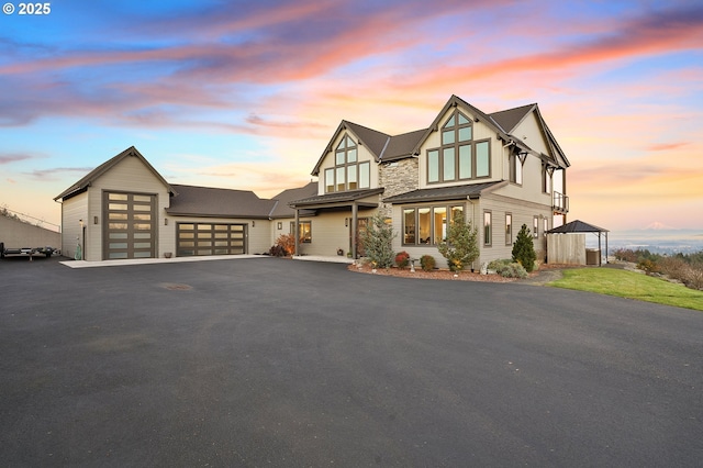 tudor home featuring an attached garage, stone siding, aphalt driveway, and board and batten siding