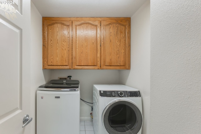 laundry area featuring separate washer and dryer, cabinets, and light tile patterned flooring