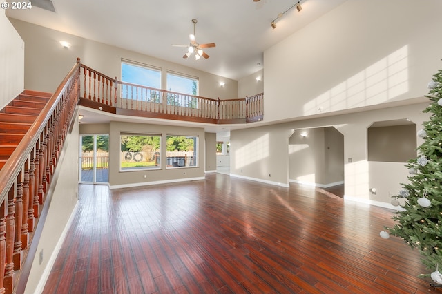 unfurnished living room with ceiling fan, a towering ceiling, and wood-type flooring