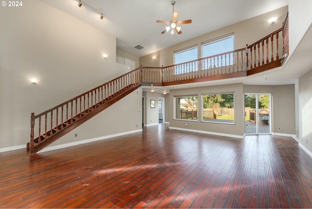 unfurnished living room with ceiling fan, a towering ceiling, and dark hardwood / wood-style floors